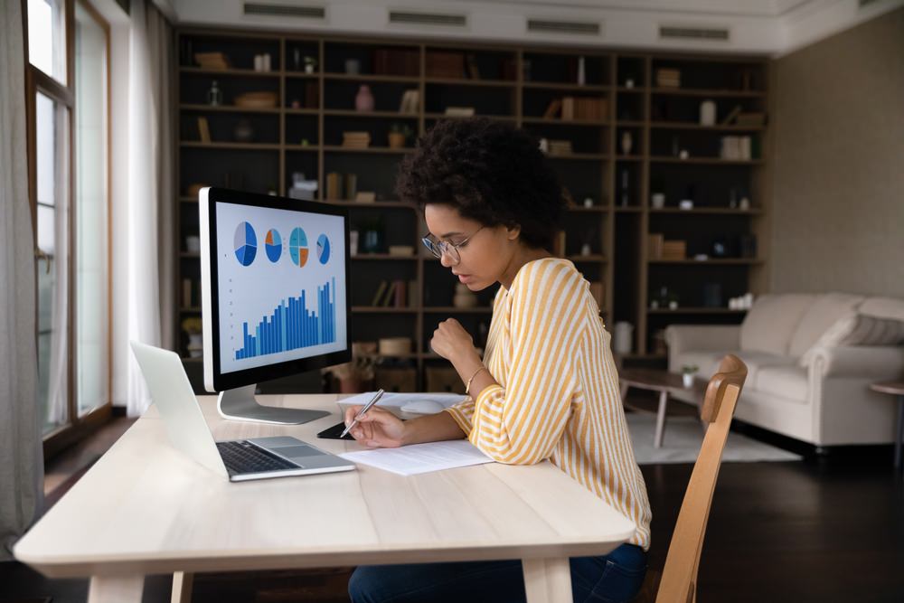 Concentrated young African American businesswoman in eyeglasses analyzing video marketing analytics on computer.